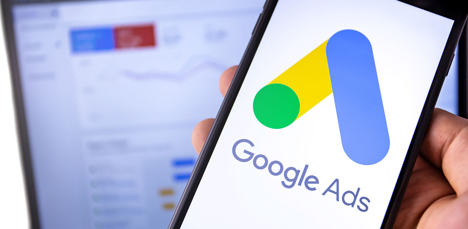 Smartphone mit Google Ads Logo und Laptop im Hintergrund